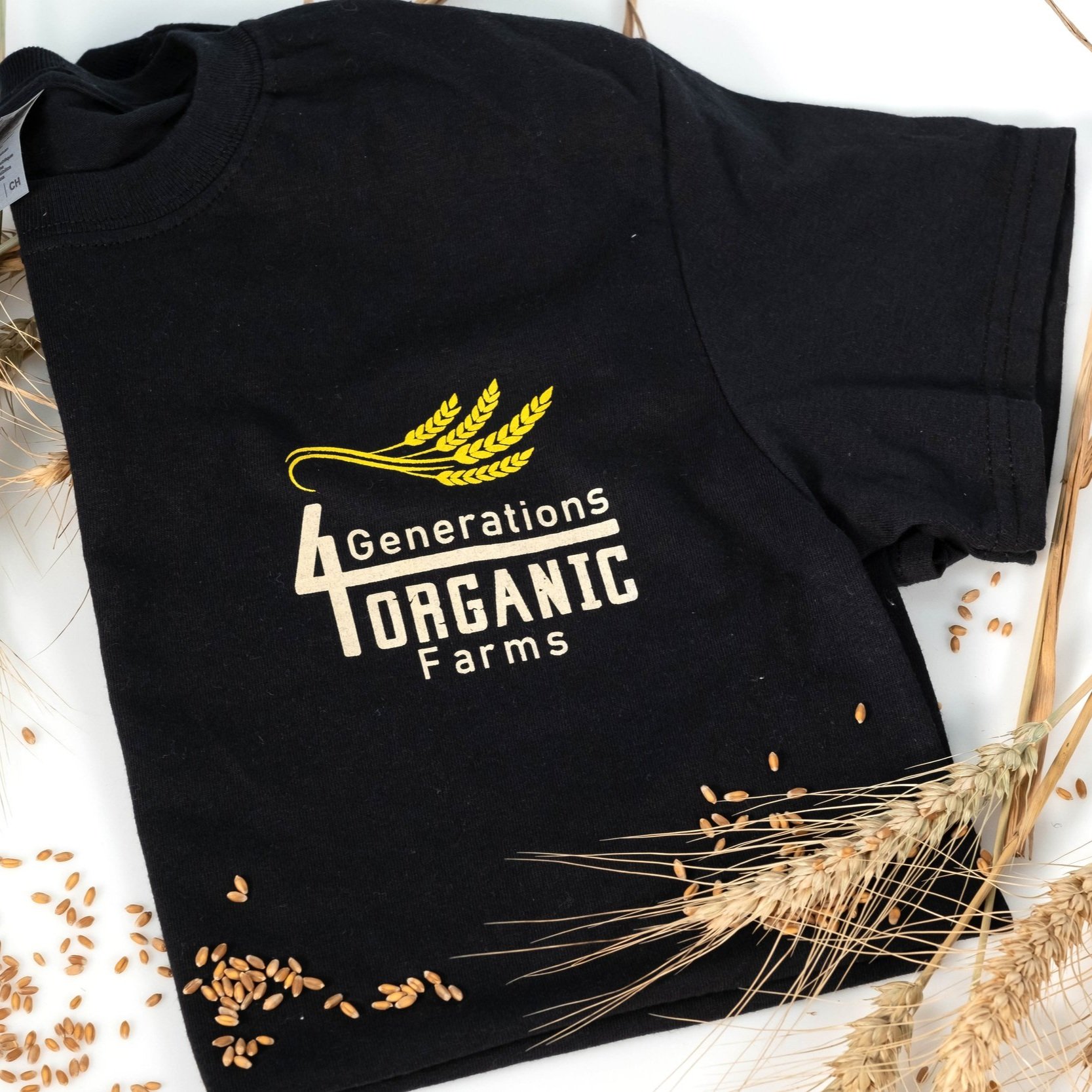 Black t-shirt featuring the logo of 4 Generations Organic Farms, surrounded by wheat stalks and grains, emphasizing organic farming and sustainability.