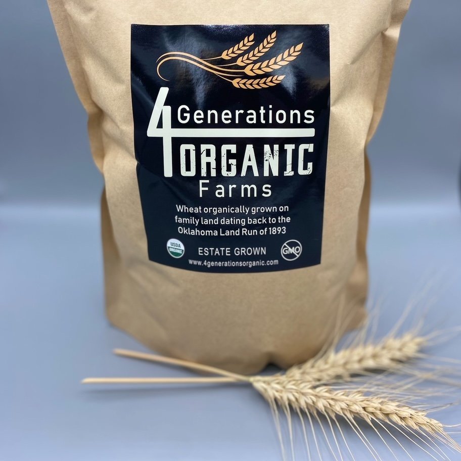 Brown paper bag of organic wheat from 4 Generations Organic Farms, showcasing a label that highlights its heritage and organic certification, with wheat stalks in the foreground.